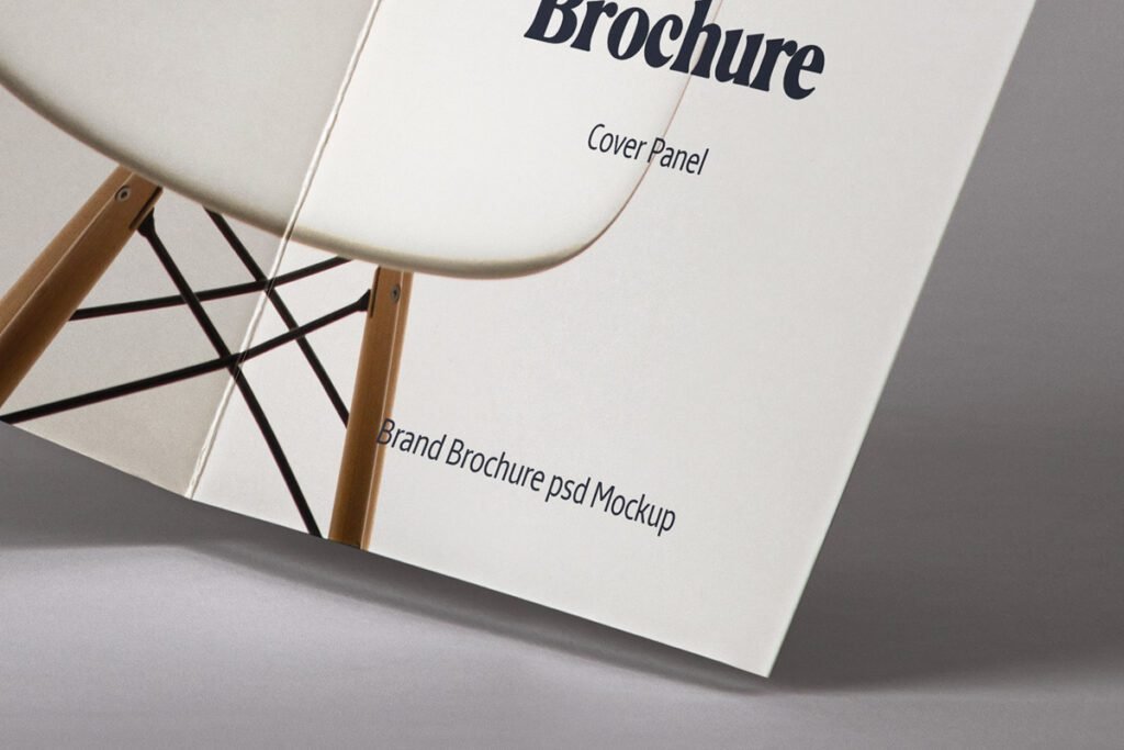 Close-up of a brochure cover panel mockup displaying "Brochure," "Cover Panel," and "Brand Brochure psd Mockup" text, with a blurred chair in the background.