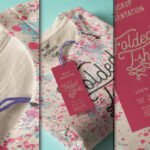 Folded white t-shirt mockup with pink and blue paint splatters and a red "Folded T-shirt" tag with washing instructions.