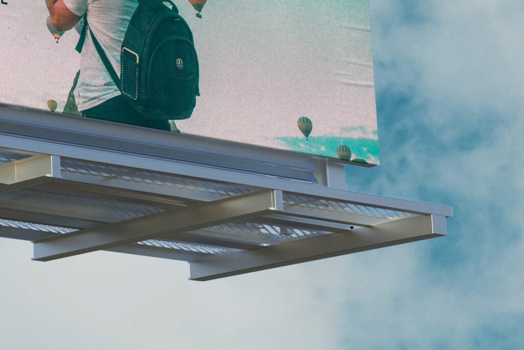 Bottom view of a large outdoor billboard displaying a partial image of a person with a backpack and hot air balloons against a cloudy sky.