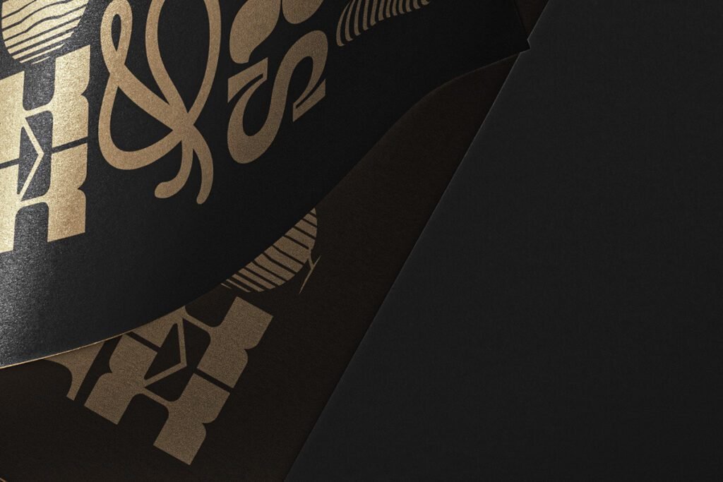 Gold foil print mockup on black paper with overlapping layers, showcasing luxurious typography and design elements.