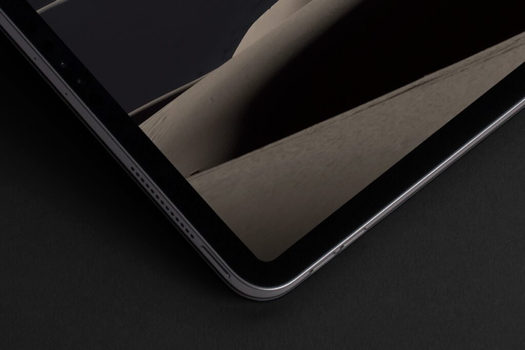 Close-up of the corner of an iPad Pro showing the screen with a desert landscape and the metallic edge on a dark surface.