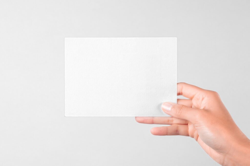 Hand holding a blank white horizontal postal card or greeting card template against a plain light background, ready for design.