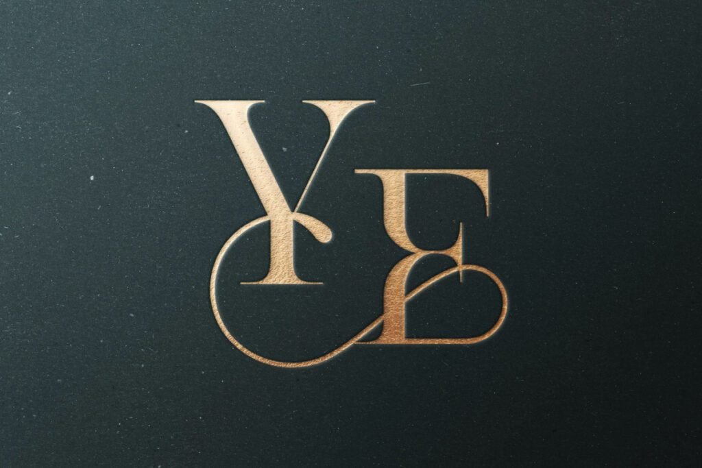 A gold pressed monogram of intertwined letters 'Y' and 'E' or 'R' on a dark, textured background, creating a luxurious and debossed effect.