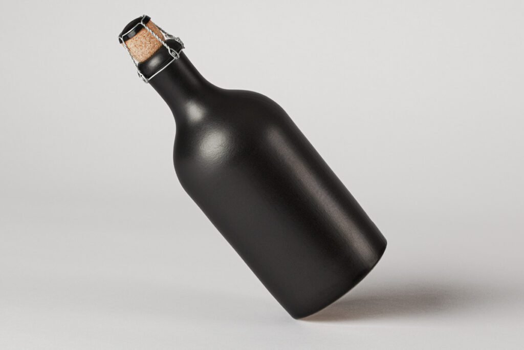 A floating black matte bottle with a cork and silver wire cage, positioned diagonally against a plain light gray background, ready for branding.