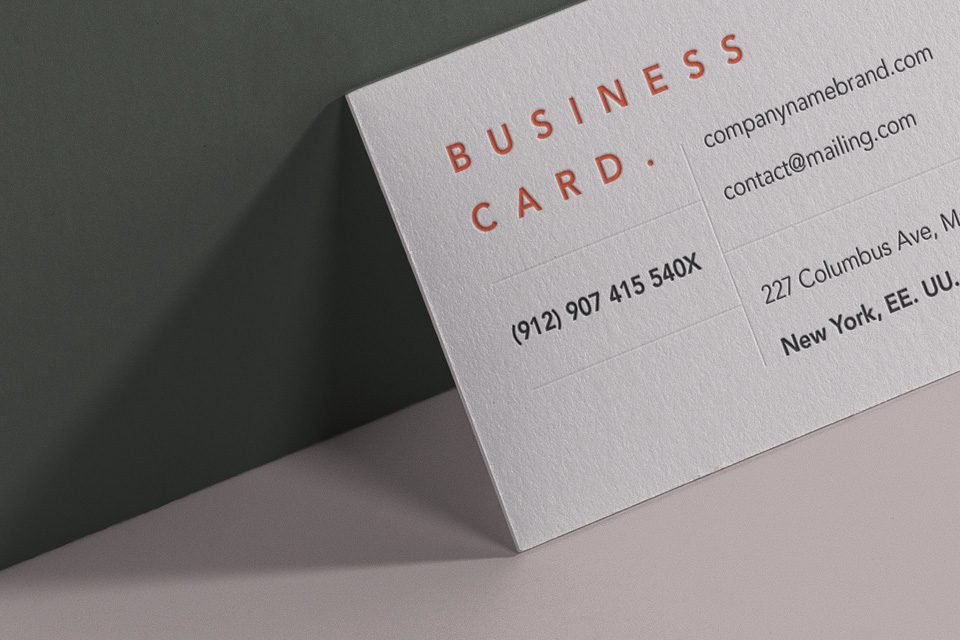 A close-up, angled view of two Wall Perspective Business Card Mockup PSD; one off-white with black text and "BUSINESS" in orange, and another salmon pink with "BUSINESS CARD" in white. They are positioned as if on a wall.