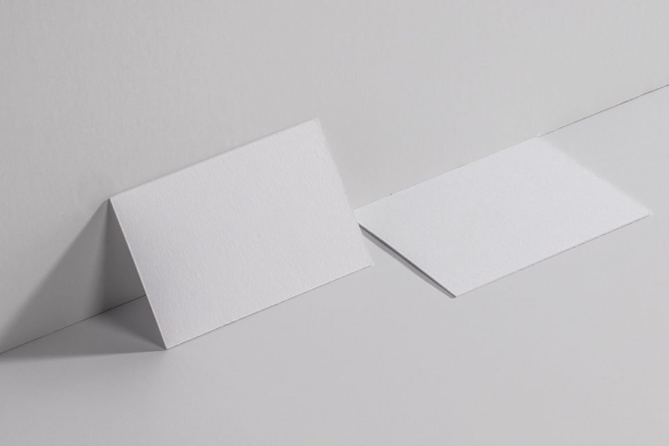 Two blank white business cards, one leaning against a light grey wall and the other lying flat beside it, showcasing a clean, minimalist mockup.