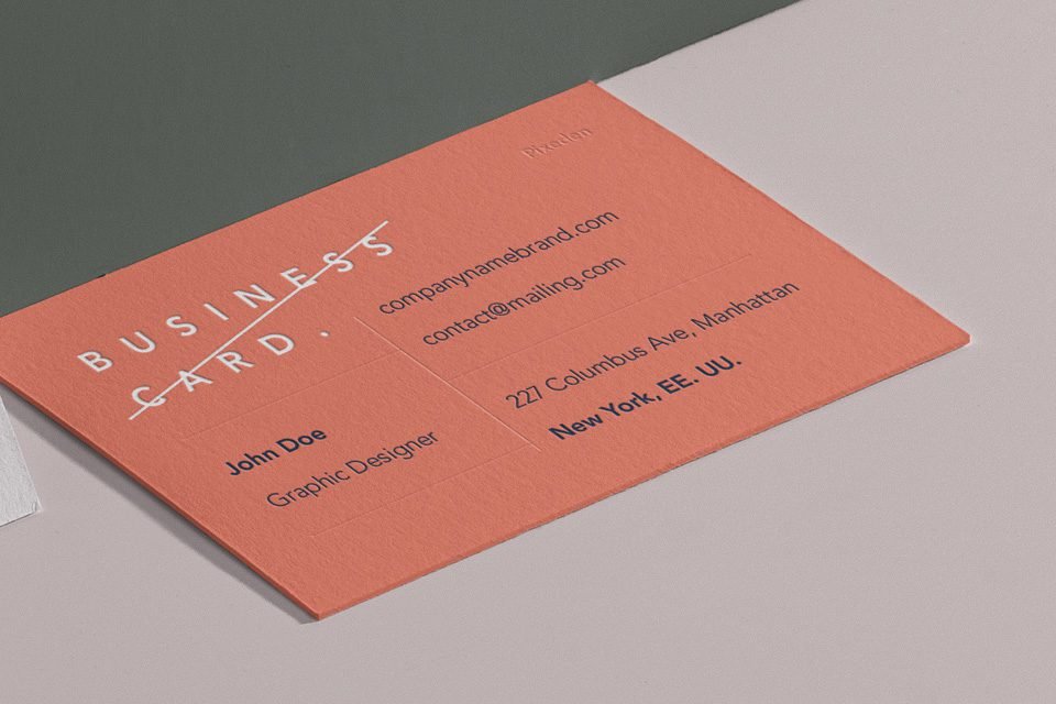 A close-up, angled view of a salmon pink business card displaying "BUSINESS CARD" in white text, alongside a name, title, and contact information, positioned on a light grey surface.