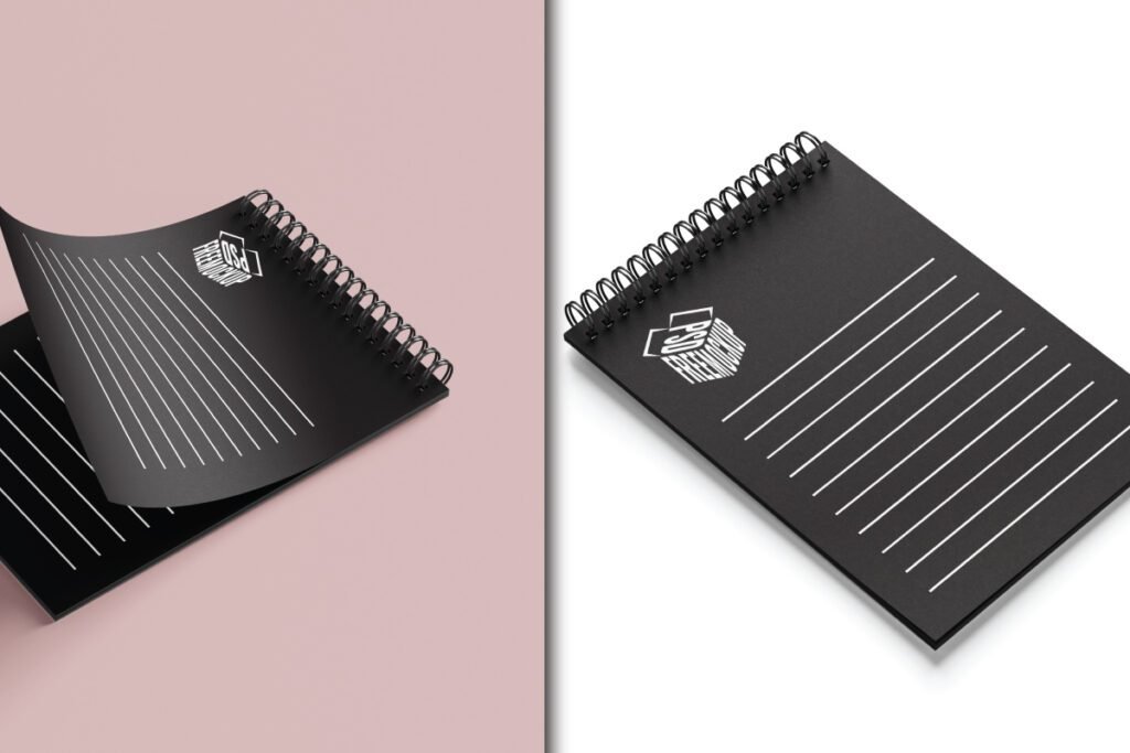 Minimalist Spiral Notebook Mockup PSD displays a black spiral notebook with a golden spiral binder and a white rectangular PSD FREEMOCKUP box logo on the cover. White ruled lines are also visible. The notebook is presented on a soft pink background.