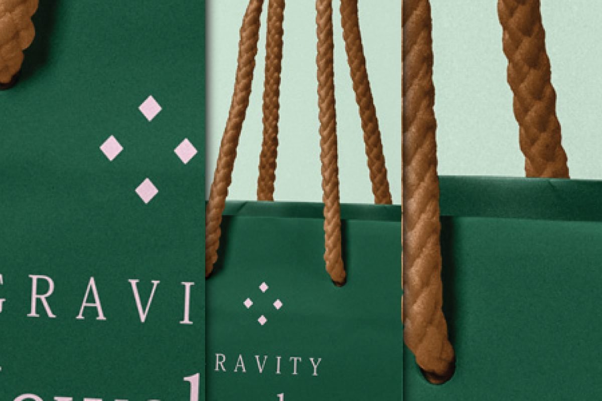 A close-up of a dark green paper bag mockup featuring a white geometric logo and part of the word "GRAVITY," with prominent brown rope handles.