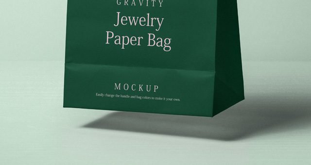 A dark green paper bag mockup standing upright, featuring "GRAVITY Jewelry Paper Bag" branding in white and pink, with a "MOCKUP" label at the bottom.