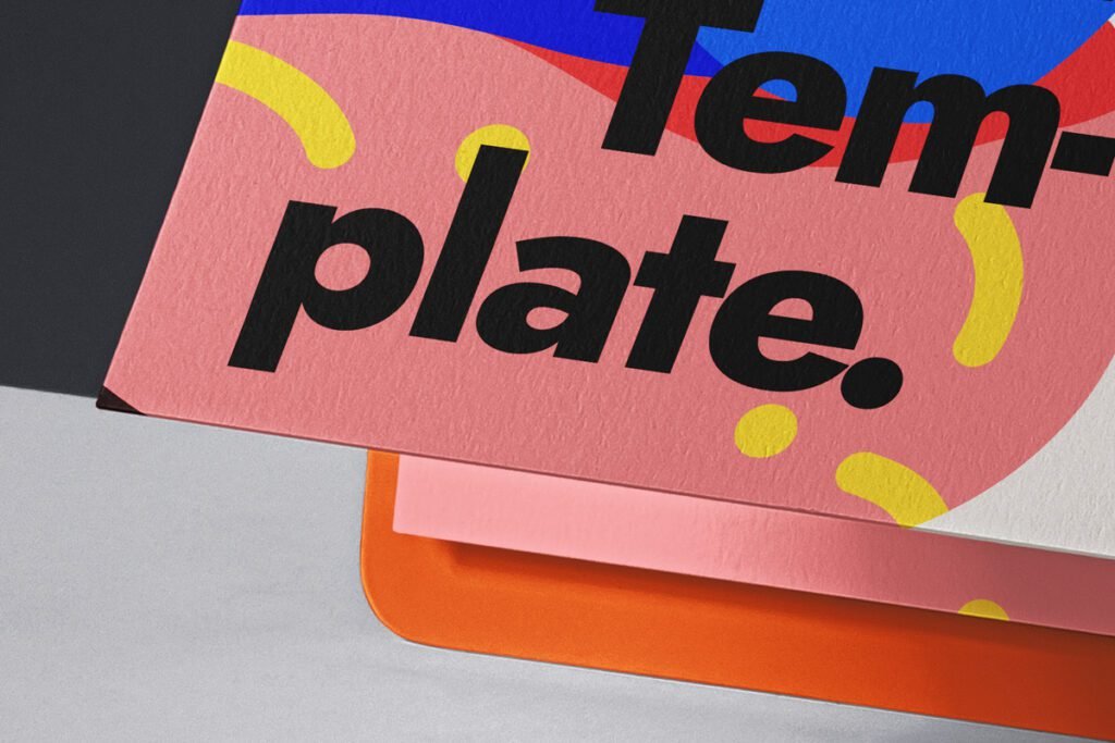Close-up of a stack of colorful textured papers, with the top sheet being pink with yellow dots, blue and red shapes, and black text "Template." visible, angled against a dark background.