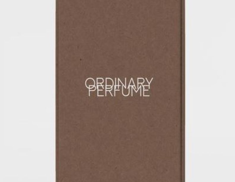 A close-up, front view of a textured brown perfume packaging box mockup with "ORDINARY PERFUME" branded in white, sans-serif text centered on its surface.