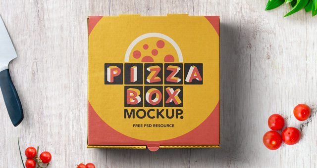 Top-down view of a colorful retro-styled pizza box on a light wooden surface, surrounded by kitchen items like cherry tomatoes, a knife, and green leaves. The box features "PIZZA BOX MOCKUP" and a pizza graphic.