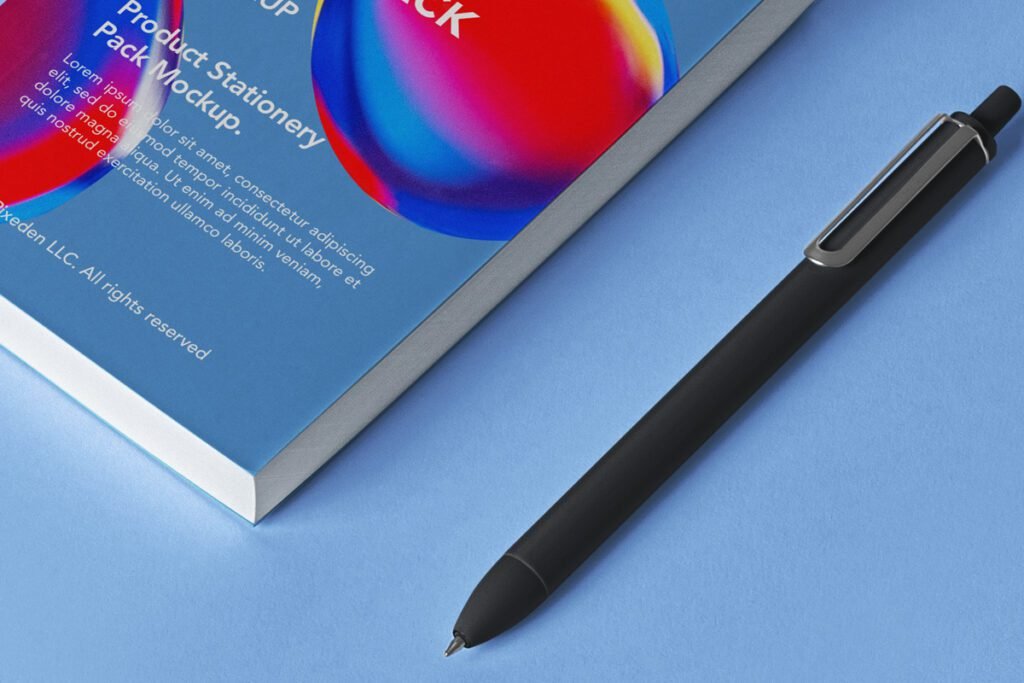 Close-up of a blue book or product box labeled "Product Stationery Pack Mockup" with colorful abstract design, next to a black pen, on a blue surface.