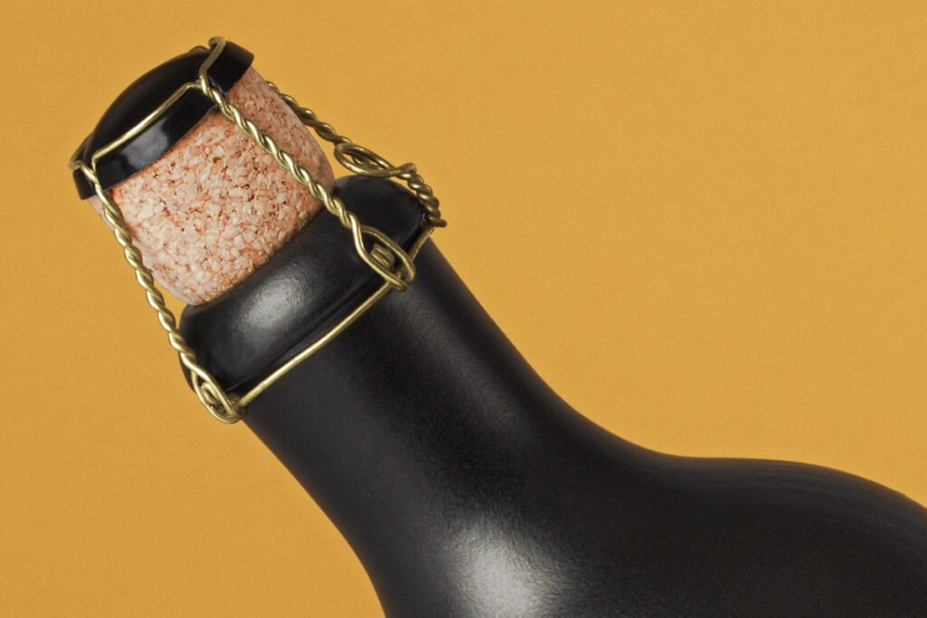 A close-up of a matte black bottle neck with a natural cork and a gold wire cage, set against a warm yellow background, ideal for a Dark Bottle Mockup PSD.