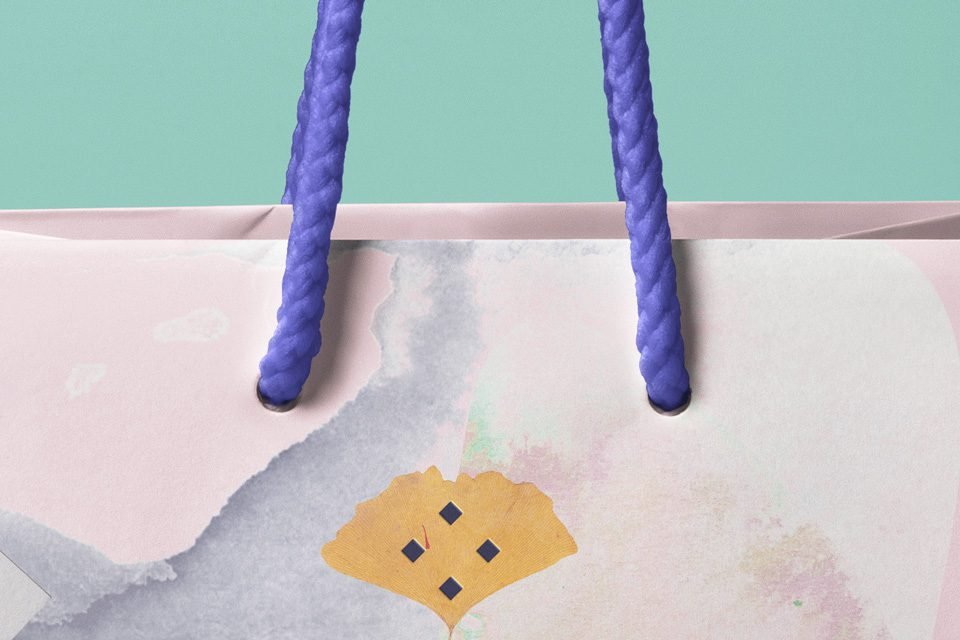 A close-up of a "Shopping Bag Mockup PSD" featuring the top of a light pink paper bag with watercolor-style grey and pink splotches, purple rope handles, and a yellow ginkgo leaf design, against a teal background.