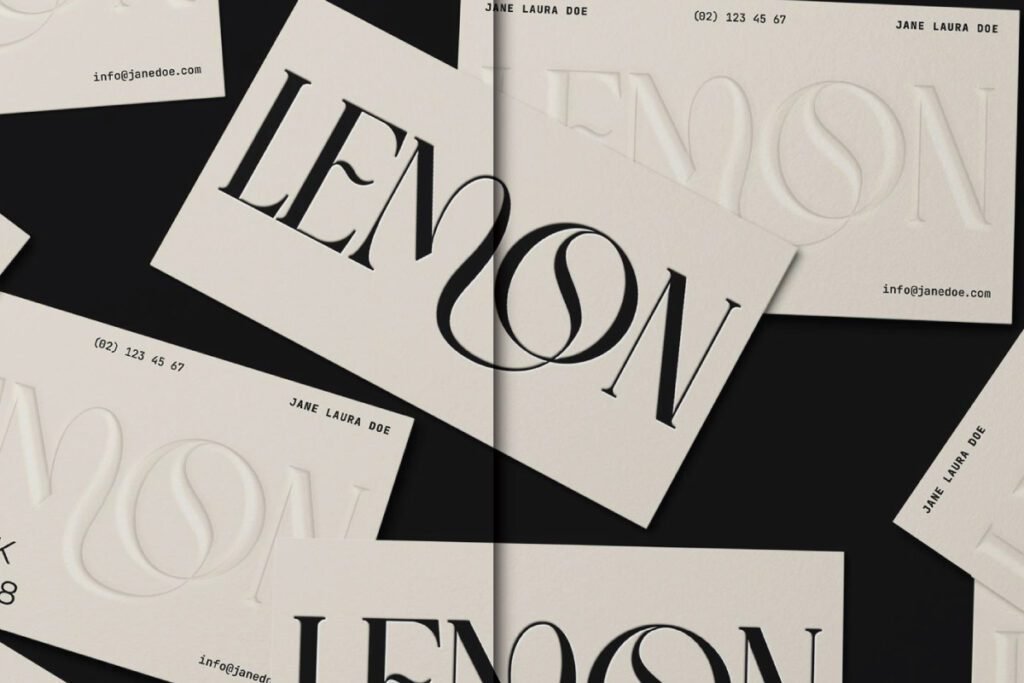 A scattered arrangement of light-colored business cards with "LEMON" text in a large stylized font, some showing an embossed effect and others with black print, alongside contact details.