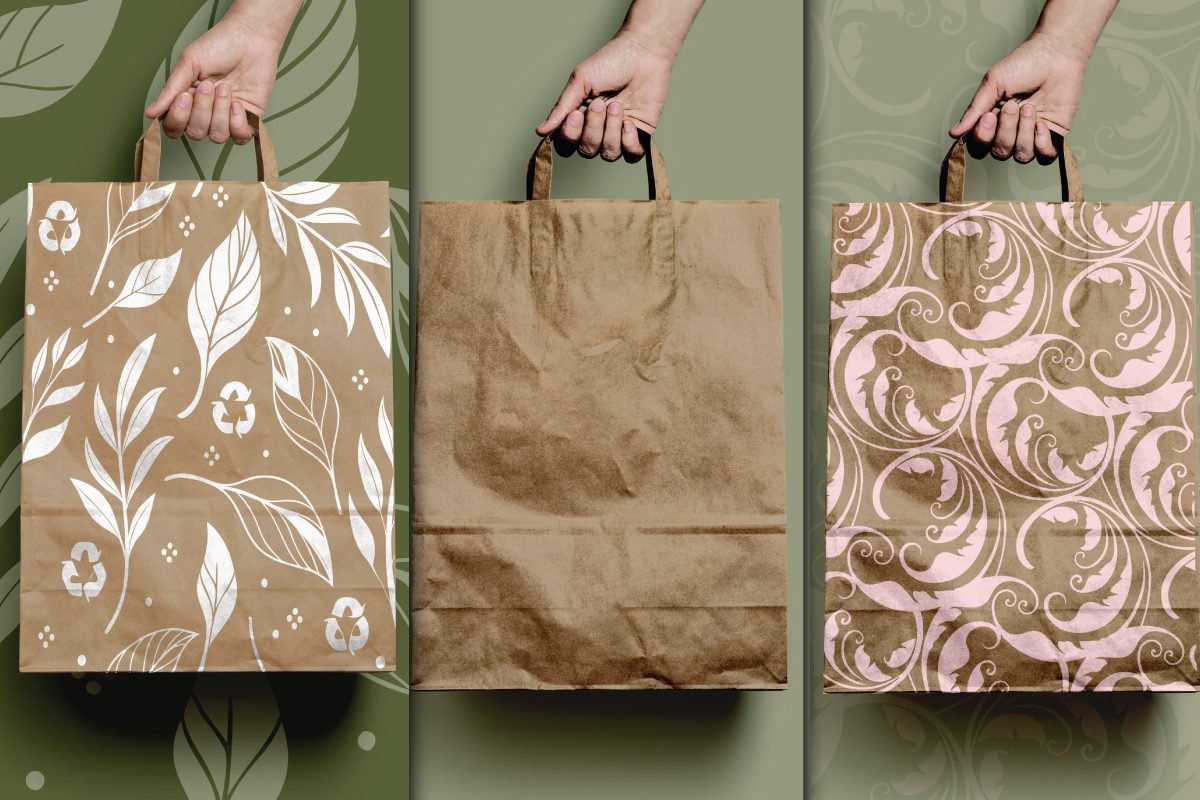 Best Zero Waste Eco Paper Bag Mockup PSD displays three hands holding brown paper bags. One bag has a white leaf pattern with recycle symbols. The middle bag is plain. The third bag has a light pink ornate pattern.
