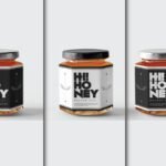 A set of three hexagonal Honey Jar Mockups, each featuring a black and white "Hi! Honey" label. The jars are filled with amber-colored liquid and have metallic or black lids, presented against a clean white background.