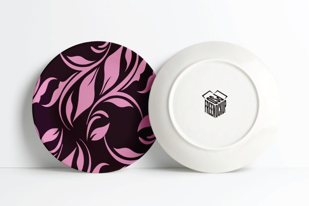 Best Realistic Ceramic Plate Wrap Mockup PSD displays a dark plate with a pink floral pattern next to a white plate showing its underside with a black box logo.